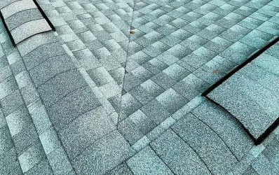 A technician from a Roofing Company in St Petersburg applying sealant under asphalt shingles to repair a roof leak.