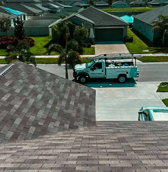 High-angle view from a rooftop showing a service vehicle parked at a job site, representing a professional Roofing Company in Tampa working in a residential neighborhood.