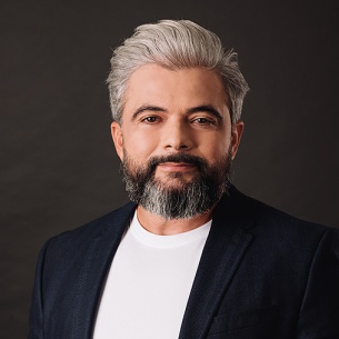 Professional portrait of Edson, a specialist from Protect Preserve Roofing, wearing a dark blazer and white shirt against a gray background.