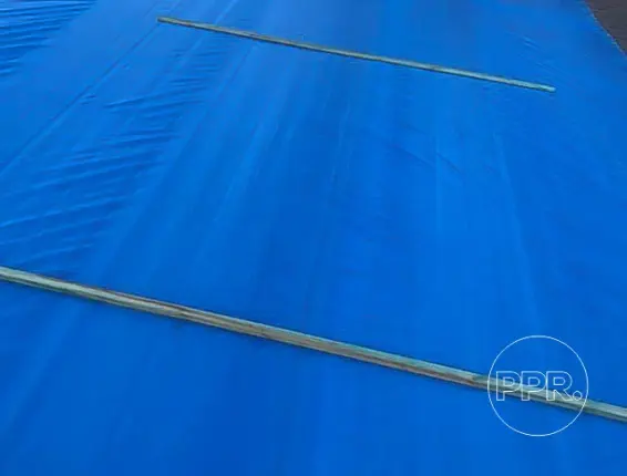 Close-up view of a blue tarp secured with wooden battens, demonstrating the mechanical attachment method used by professional emergency roof tarp service near me providers.
