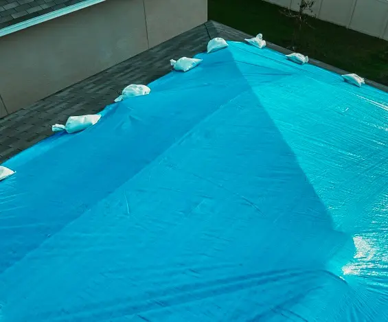 High-angle view of a blue tarp secured with white sandbags to prevent leaks, illustrating a professional emergency roof tarp service near me.