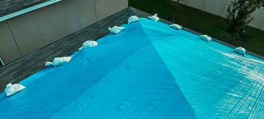 Blue emergency tarp secured with sandbags on a house roof as a temporary measure before roof repair services.