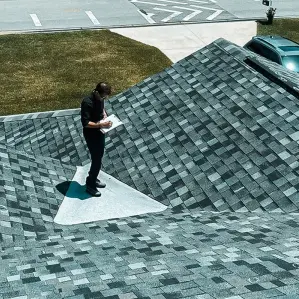 A specialist from Protect Preserve Roofing conducting a detailed roof inspection on a residential home, checking asphalt shingles for potential damage.