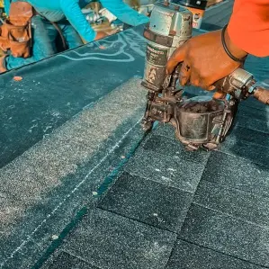Close-up of a Protect Preserve Roofing technician using a pneumatic nail gun to precisely secure asphalt shingles during a roof installation.