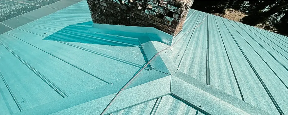 Close-up of sealed flashing around a brick chimney, demonstrating detailed metal roof repair service on a standing seam roof.
