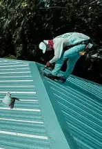 A close-up view of a caulking gun resting on the hip of a brown ribbed metal roof, illustrating the sealant application process during a metal roof repair service.