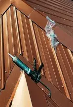 Close-up view of a caulking gun applying high-grade sealant to standing seams during a comprehensive metal roof repair service.