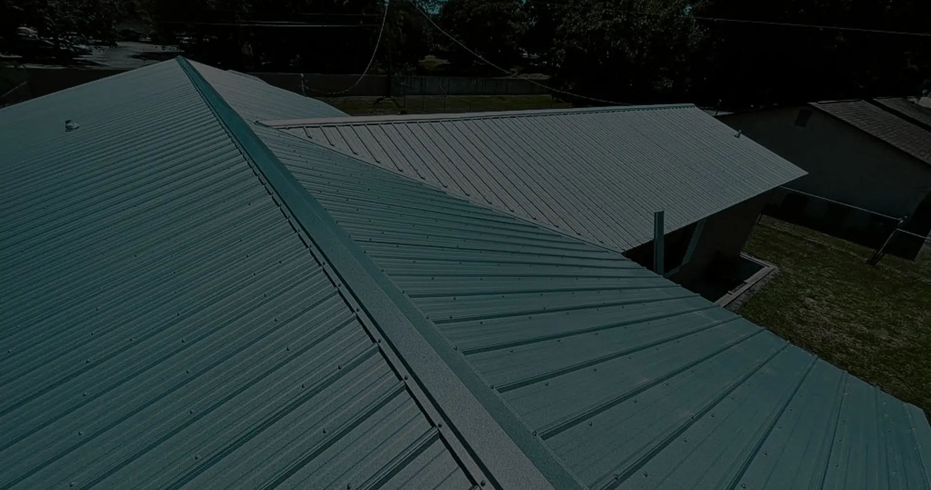 Aerial view of a residential home displaying the results of a professional metal roof repair service on green ribbed panels