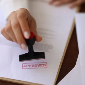 Close-up of a hand stamping 'APPROVED' on a document, representing the seamless roofing permit and insurance approval process managed by Protect Preserve Roofing.