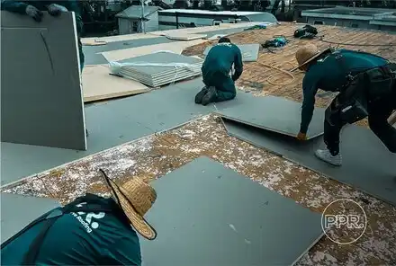 A team of Protect Preserve Roofing workers installing new insulation or underlayment panels on a flat roof during a repair project.