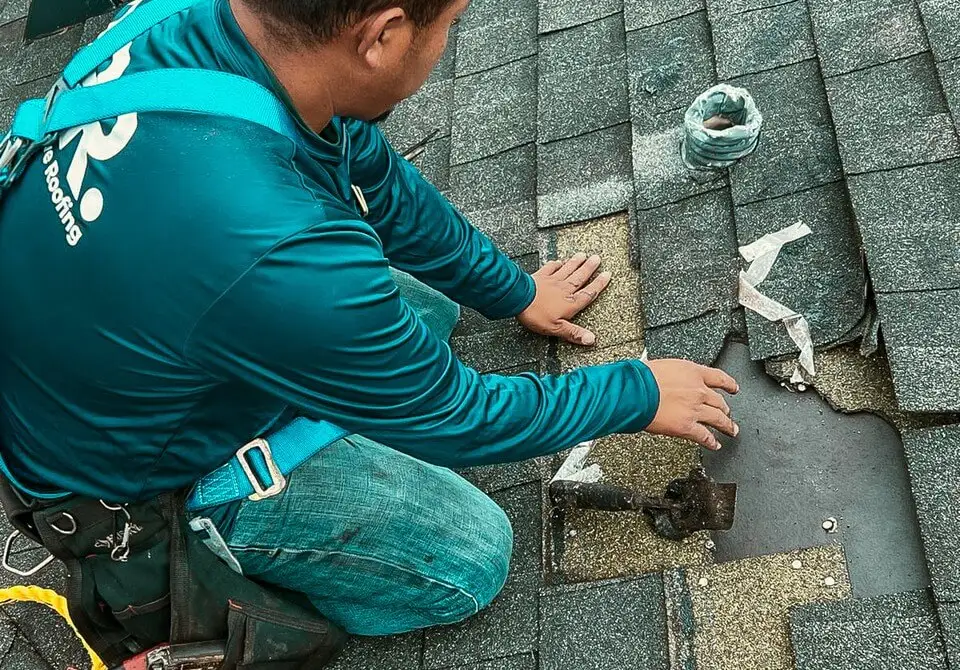 A worker from Protect Preserve Roofing kneeling to repair a damaged section of a residential shingle roof.