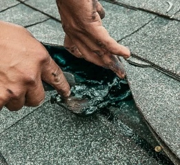 Close-up of a worker performing professional roof repair services by fixing damaged shingles with sealant.