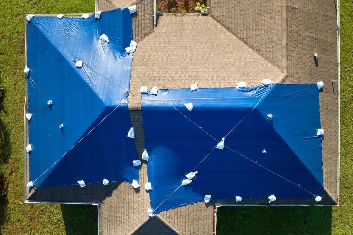 Aerial view of a residential roof covered with blue tarps and sandbags to protect preserve roofing after storm damage