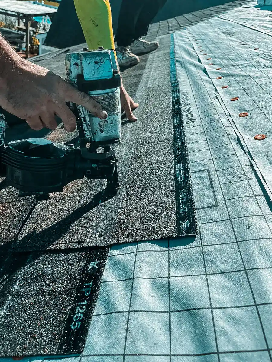 A close-up of a Protect Preserve Roofing professional using a nail gun to install new shingles over a synthetic underlayment during a roof replacement.