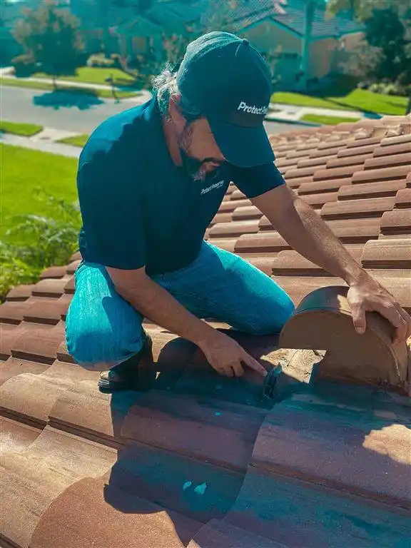 A roofing contractor from Protect Preserve Roofing is carefully working on a residential clay tile roof, likely performing maintenance or repair.