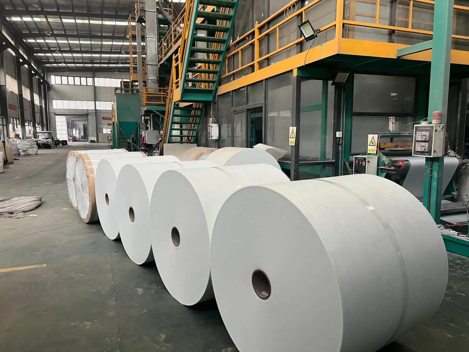 Large fiberglass mat rolls as base material for roofing shingles in a manufacturing facility.