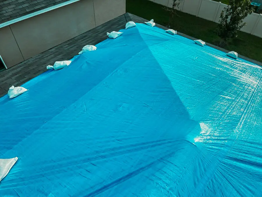 Large blue tarp secured with sandbags on a residential roof to protect preserve roofing after storm damage