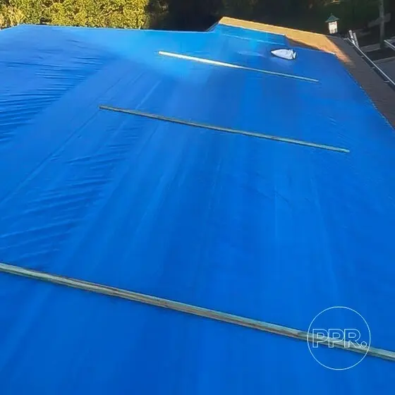 Blue tarp mechanically attached to a residential roof with wooden planks to protect preserve roofing from water damage