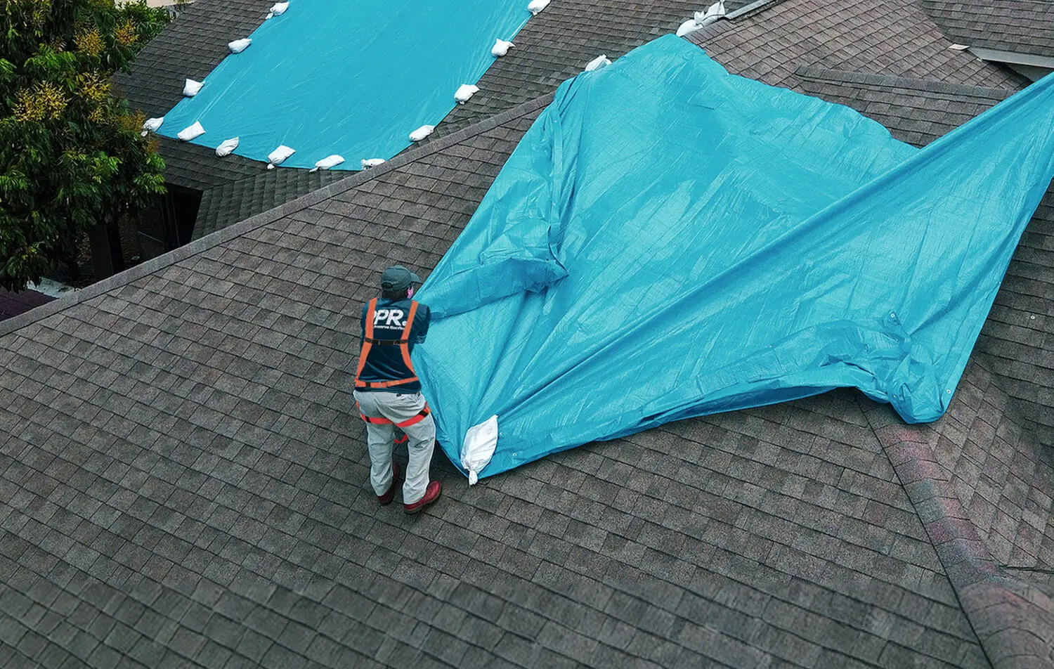 Blue tarp secured with sandbags on a residential roof to protect preserve roofing from further damage