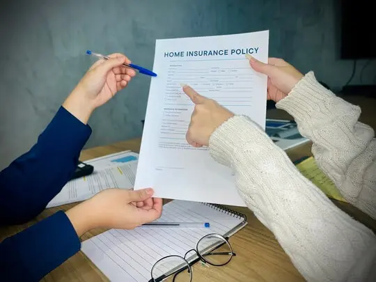 Couple reviewing a home insurance policy with an agent, discussing if coverage will protect preserve roofing with a tarp installation