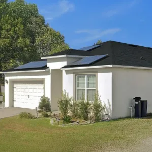 A modern white house with a new black shingle roof and solar panels, showing the result of roof replacement financing made simple.