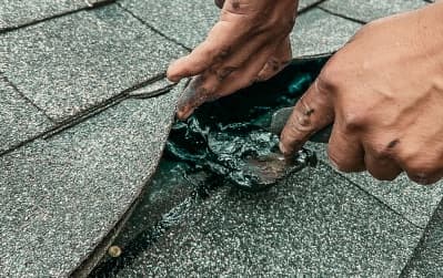 Close-up of a professional worker repairing damaged shingles on a roof, representing roofing companies in Clearwater.