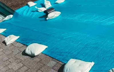 Blue emergency tarp secured with sandbags on a damaged roof – emergency services provided by our roofing company central florida.