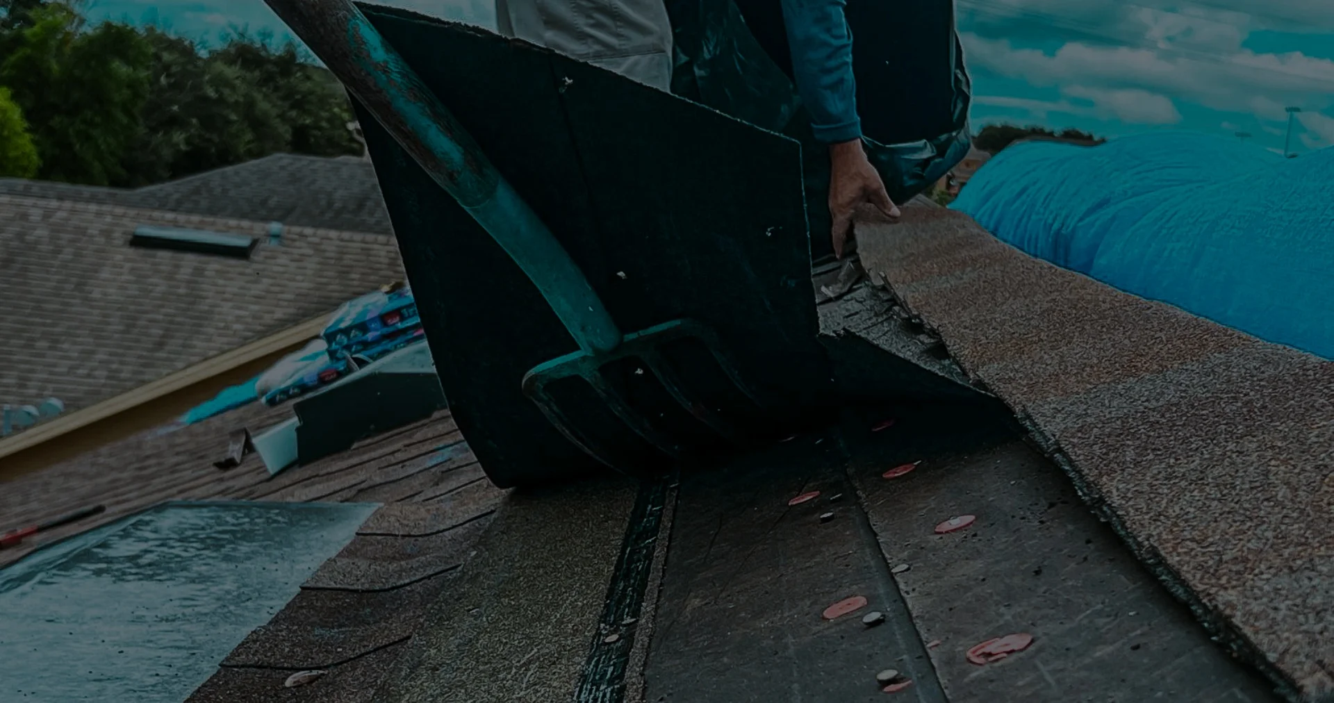 Roofing company Florida crew member actively removing old asphalt shingles from a residential roof using a tear-off fork tool.