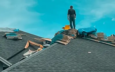 Roofer standing on a residential roof with bundles of shingles during a replacement project by our roofing company St Cloud.