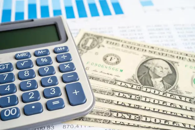 Calculator and dollar bills on financial documents, representing cost estimation to protect and preserve roofing through proper budgeting.