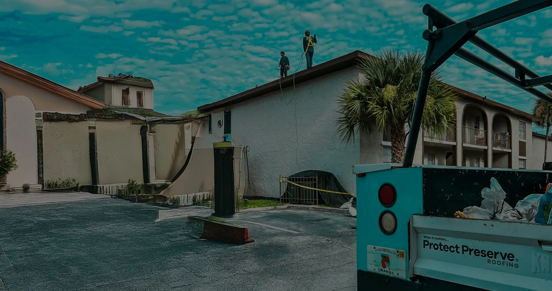 Two professional roofers working on a white building under a blue sky, with a Protect Preserve Roofing truck in the foreground. This is a great time to schedule a roof inspection in florida.