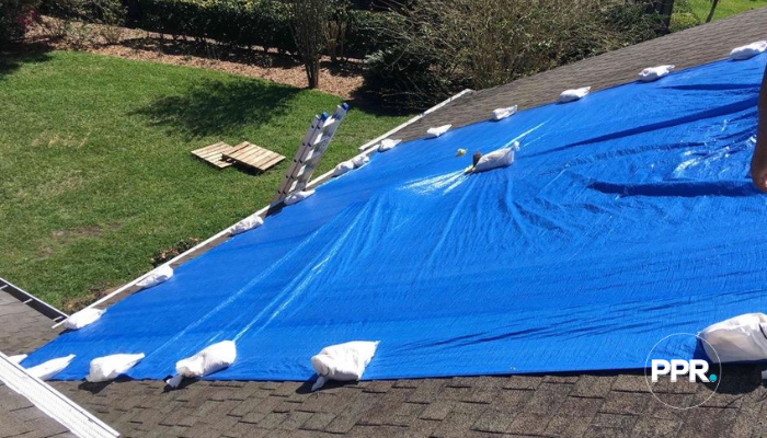 Blue roof tarp installed and secured with sandbags after storm damage.