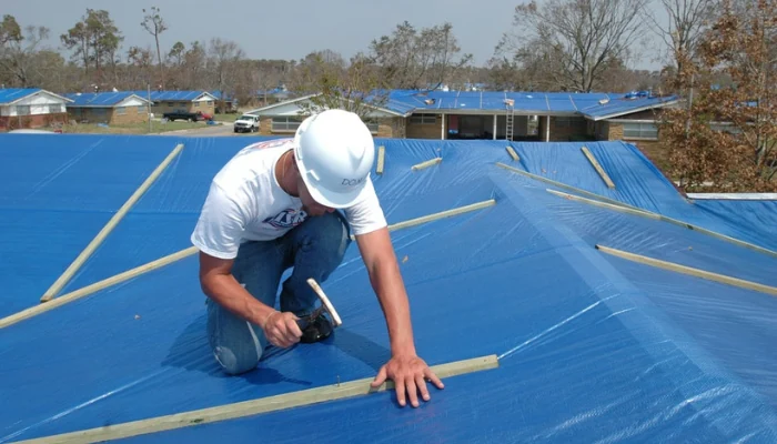 Man installing a blue tarp on the roof to represent the keyword blue tarp installed to prevent storm damage.