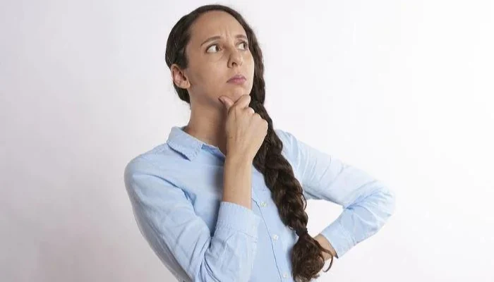 A woman with her hand on her chin thinking about what to do to represent the keyword diy or call a professional.