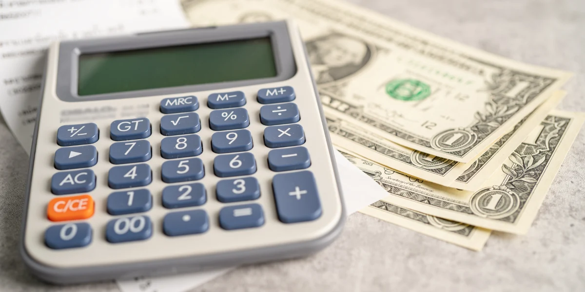 A calculator with a few dollars on a table to represent the keyword how mucha to tarp a roof.