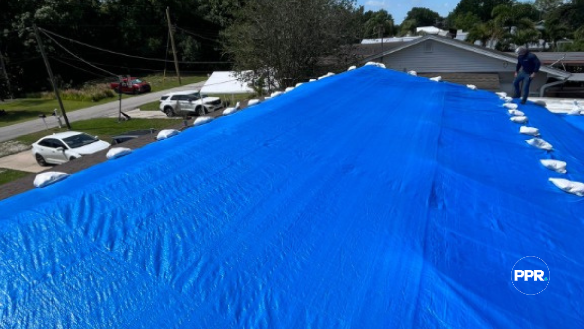 Large blue tarp installed on a residential roof and secured with sandbags to prevent storm damage.