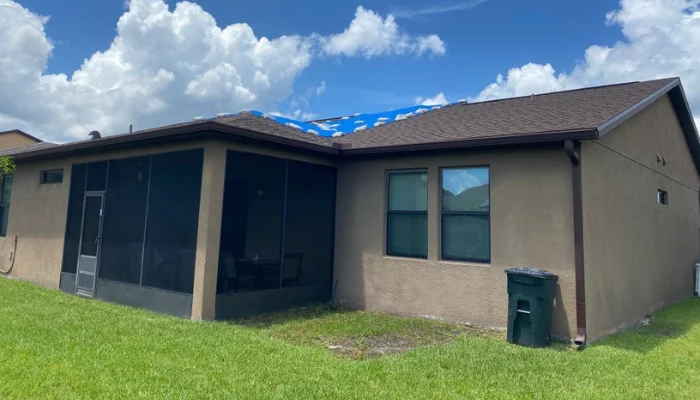 House in the countryside with a blue tarp installed to represent the keyword blue tarp installation.