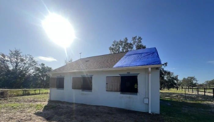A house with a blue roof and the strong sun in the background to represent the keyword blu tarp uv resistent.