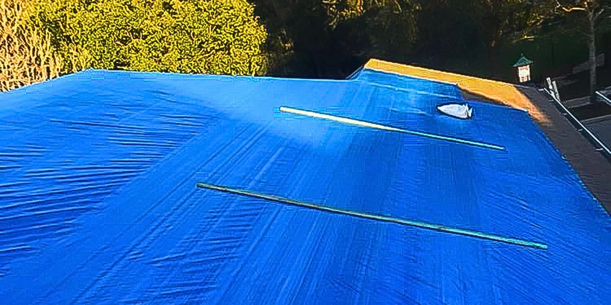A blue tarp installed on the roof in the sun to represent the keyword do blue tarps block heat.