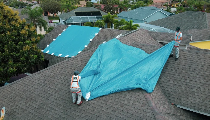 Crew installing blue tarp on a roof to represent the keyword emergency tarp fpr roof near me.
