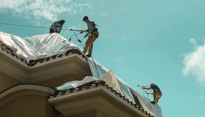 Team installing tarp on a roof safely to represent the keyword installing tarp with safety.