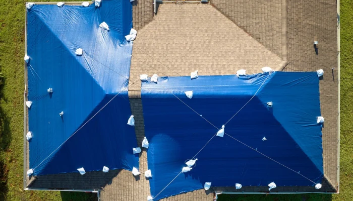 House with a roof covered by a blue tarp to represent the keyword roof tarp insurance photos.