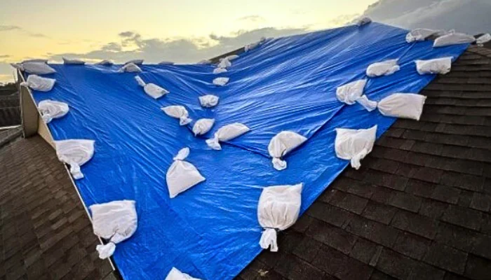 Roof with blue tarp installed with sandbags to represent the keyword roof tarping service with sandbags.