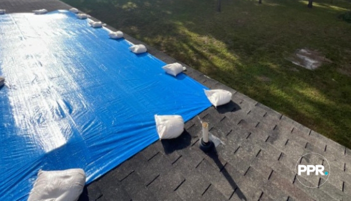 Blue roof tarp secured with white sandbags on a shingle roof.