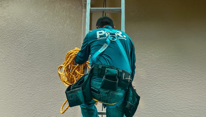 Professional descending a ladder with equipment to represent keyword roofing professional.