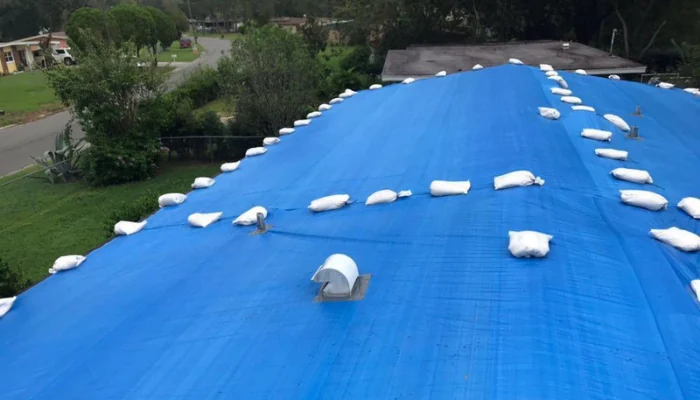 Roof with blue tarp installed without nails to represent the keyword tarping with sandbags.