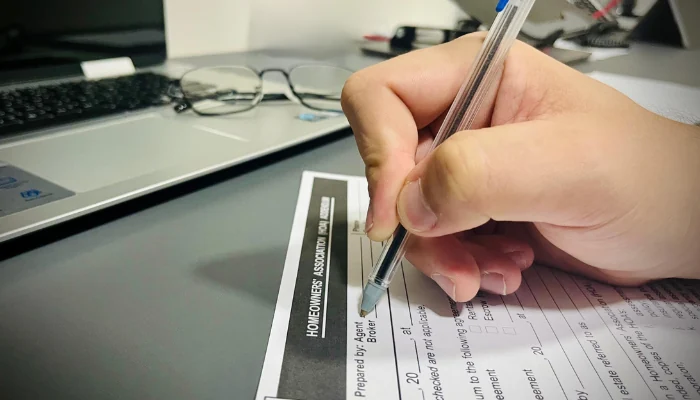 Hand signing a document on a table to represent the keyword condo roof leak.