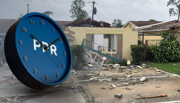 A clock next to a house with storm damage to represent the keyword time vs damage.