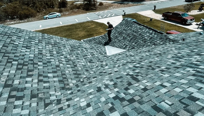A roof seen from above with a person working on it to represent the keyword architectural roof shingles vs asphalt cost.