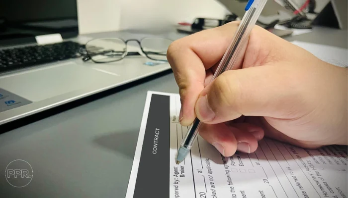 A person holding a pen to sign a contract to represent the keyword choosing a roofing contractor.